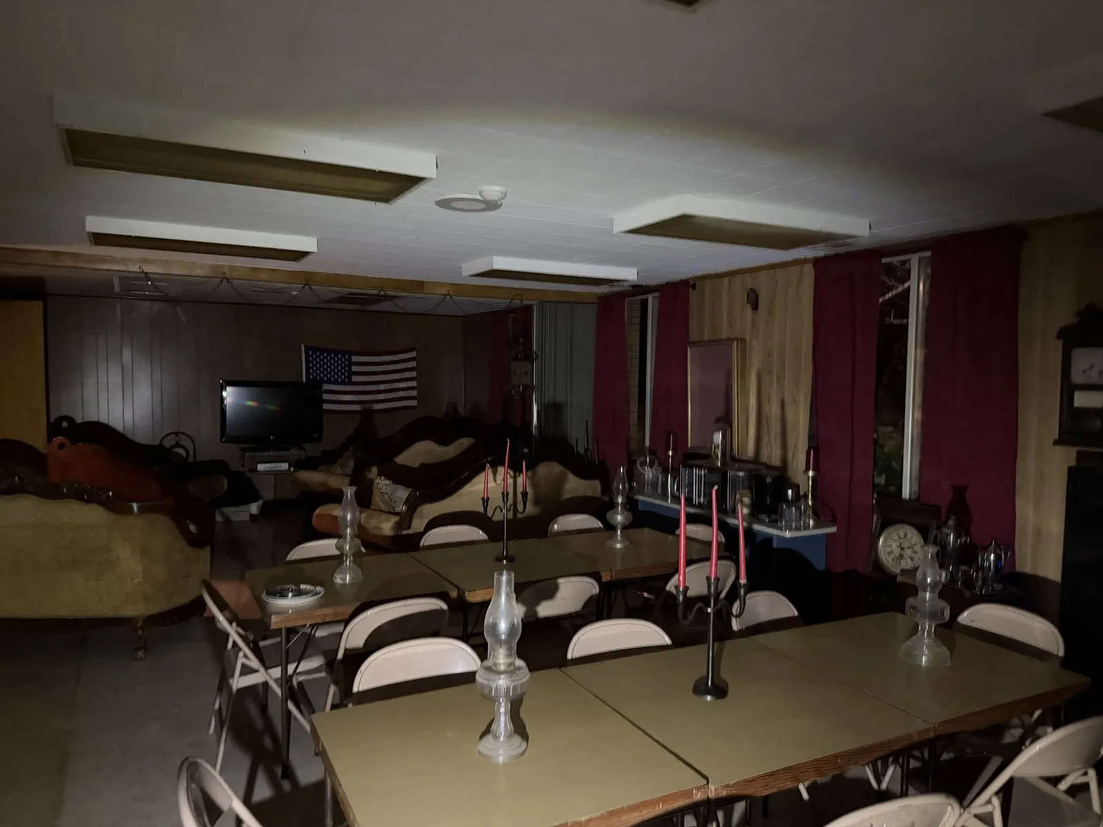Long dining tables set with oil lamps and red candles, with red curtains and Victorian sofas behind