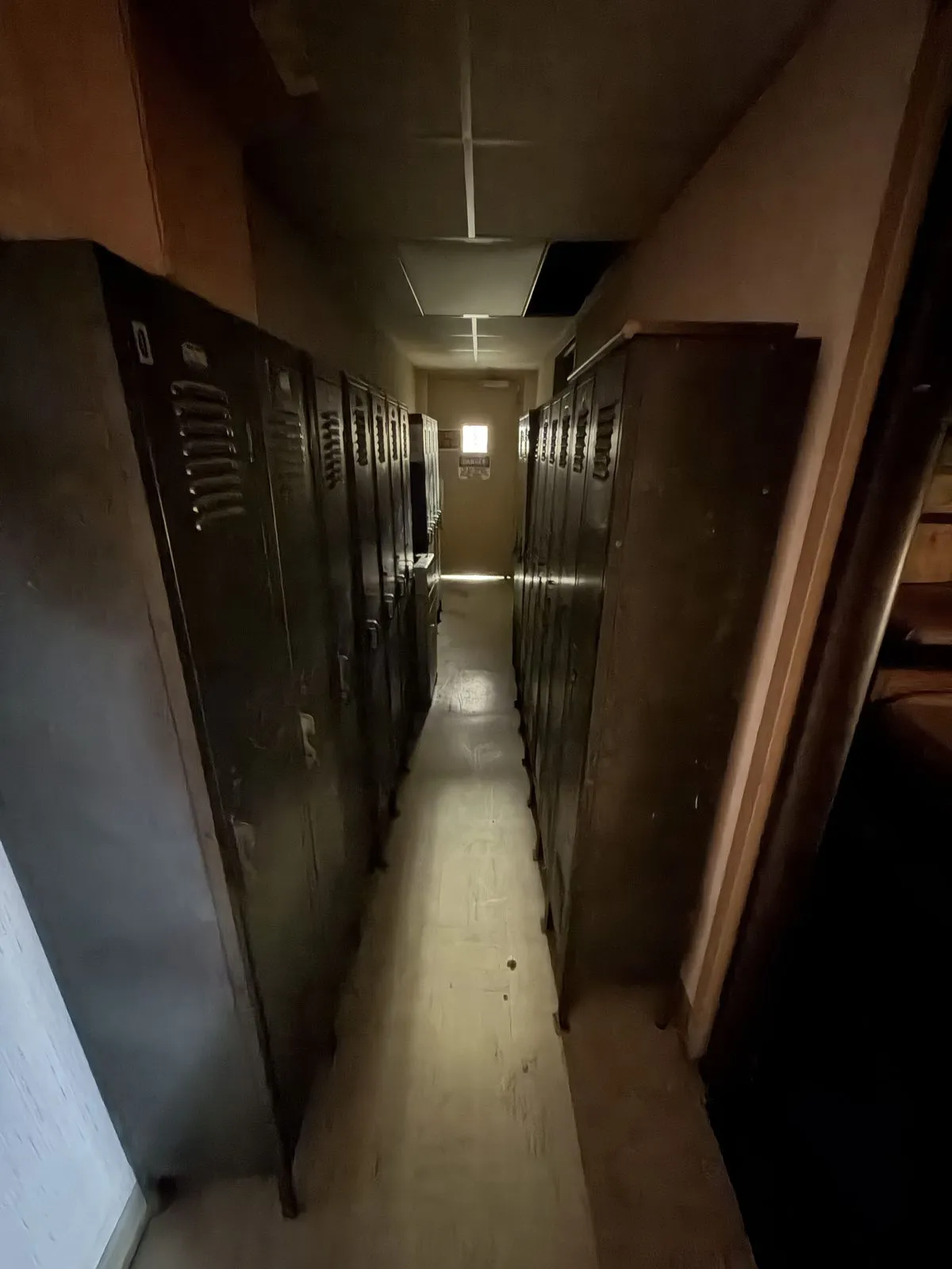 A narrow corridor lined with old metal factory lockers, fading into a faint light at the far end